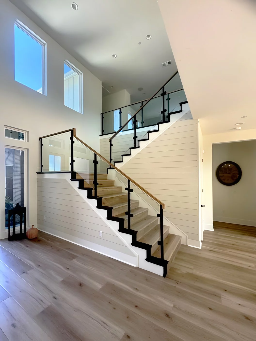 Glass railings with black iron posts and wood handrail on staircase with landing in Murrieta, California home