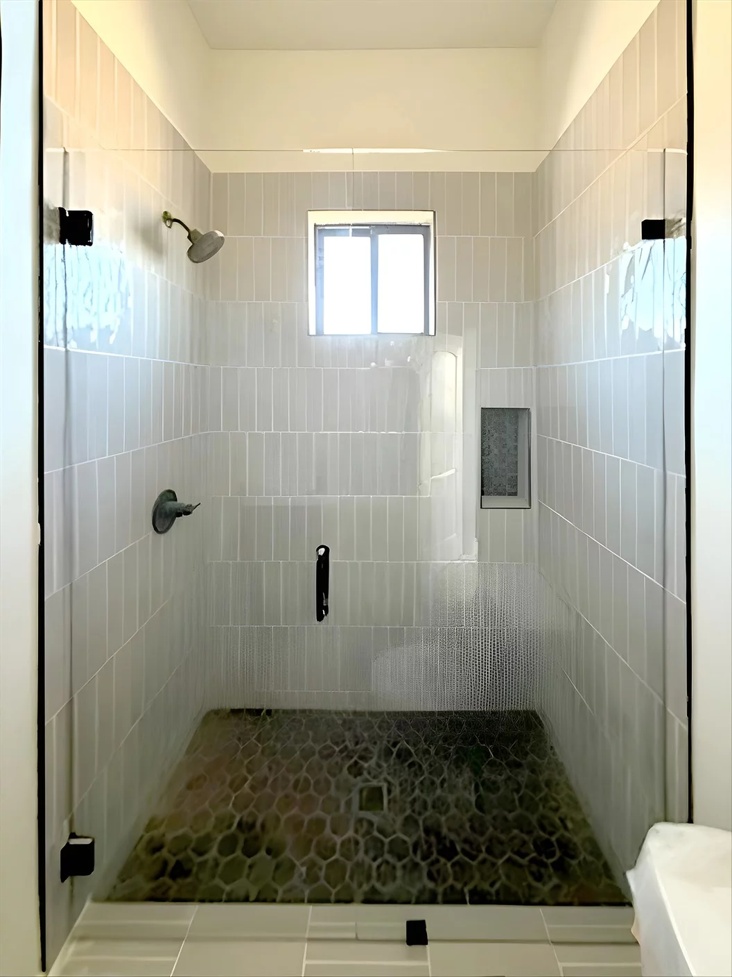Frameless glass shower enclosure with door, black handle, and clips in modern California bathroom
